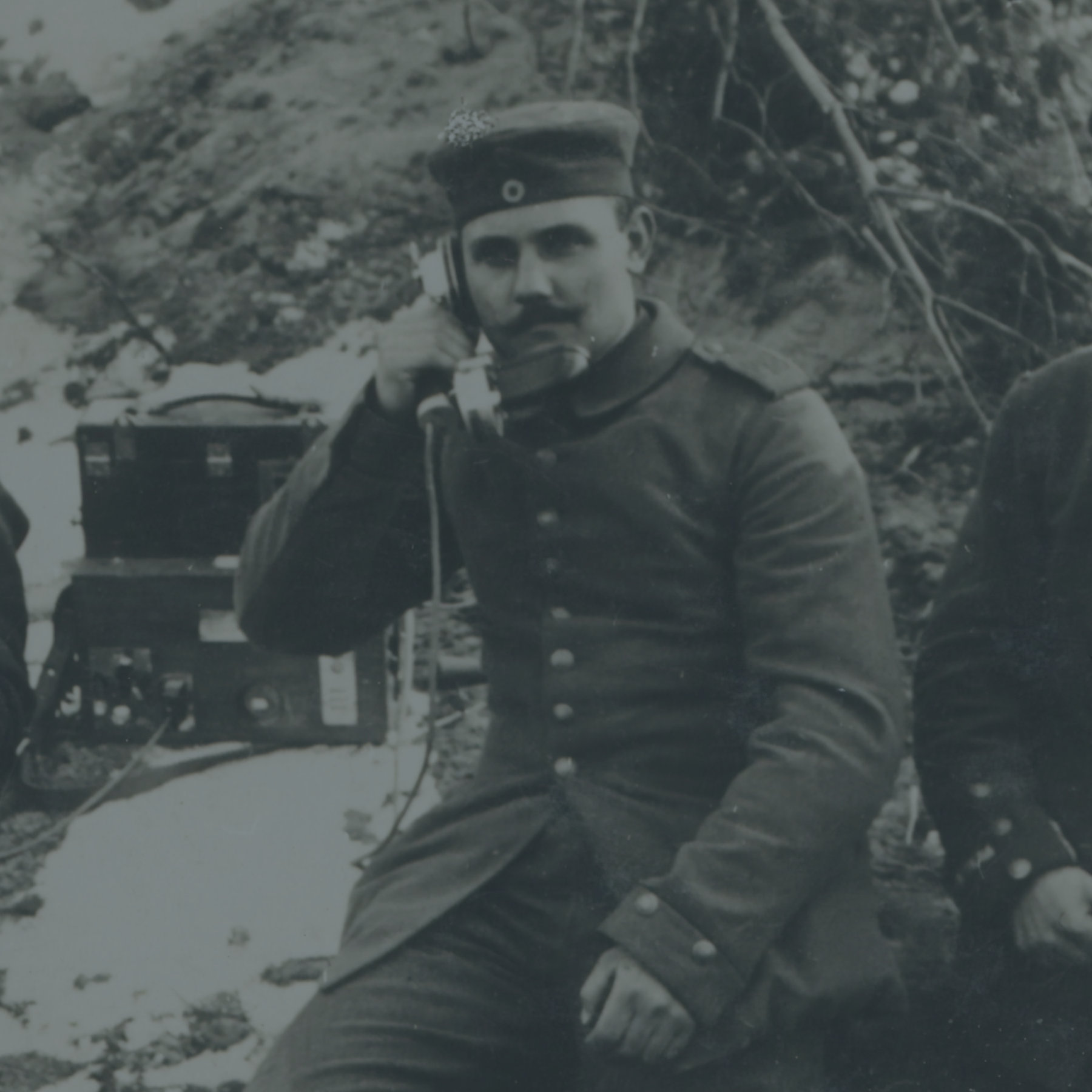 A soldier in uniform, in a trench, speaking into a telephone handset.